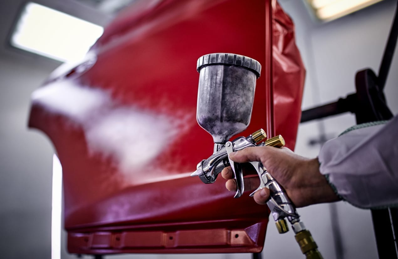 Spray gun laying a coat of red paint across a car panel in the booth