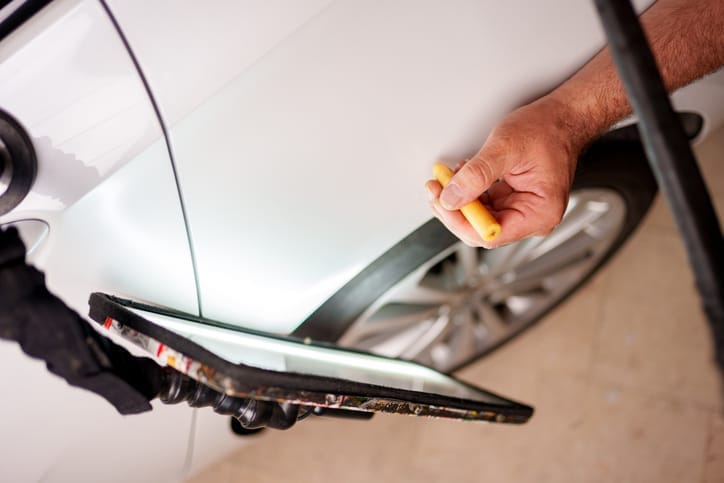 Technician working a dent out of a white door panel with a paintless dent tool
