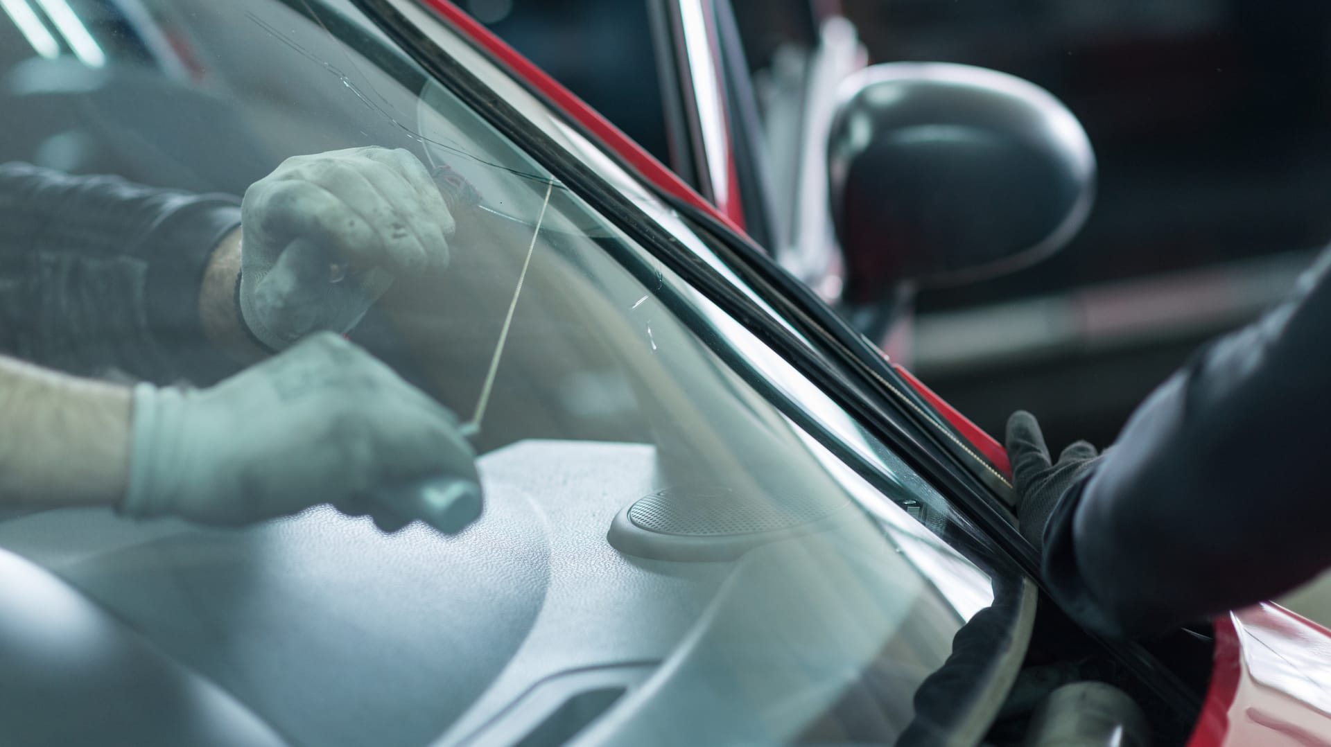 Technicians in gloves setting a new windshield into a red car