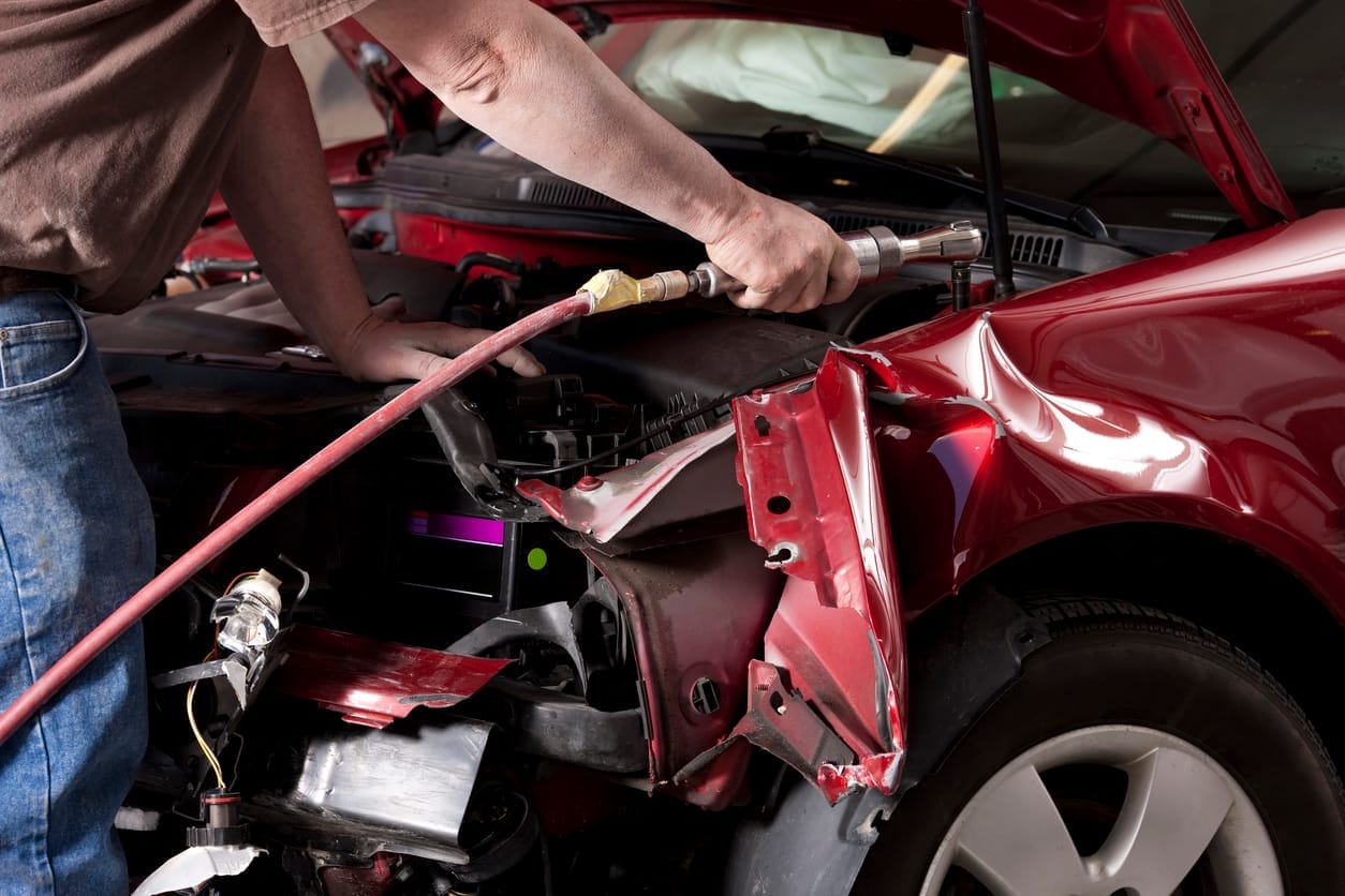 Body technician stripping crushed panels from the front of a red car