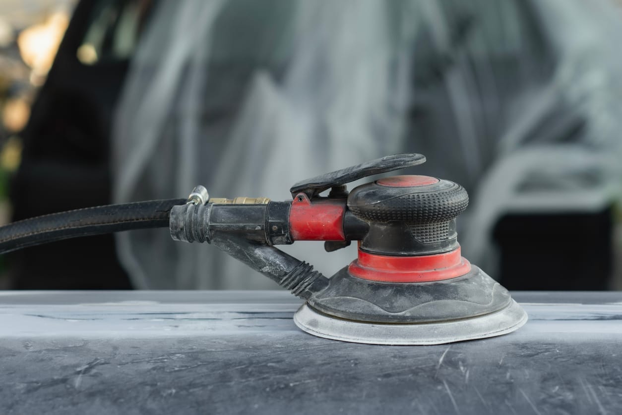 Dual-action orbital sander resting on a car panel sanded down for primer