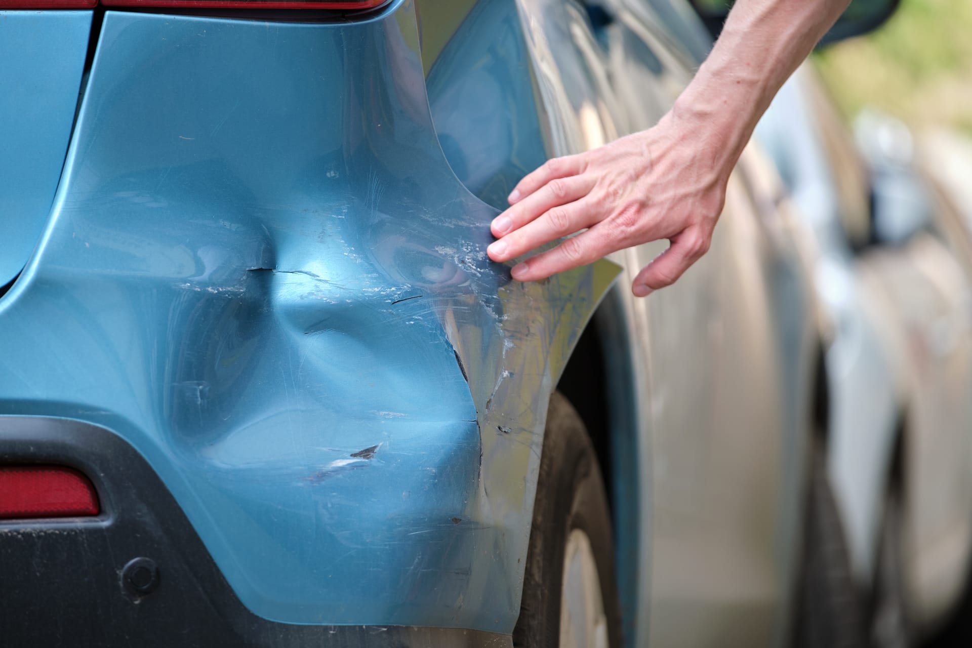 Hand resting on the creased rear quarter panel of a dented blue car