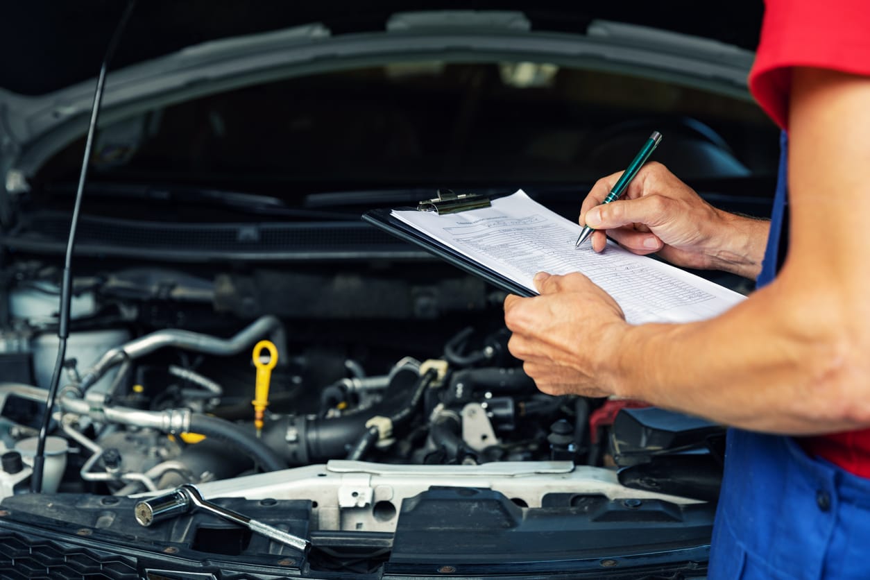 Technician writing a repair estimate on a clipboard beside an open hood