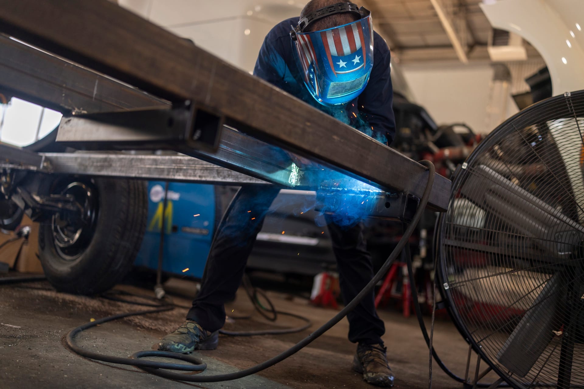 Welder in a helmet joining a metal frame section with a bright blue arc