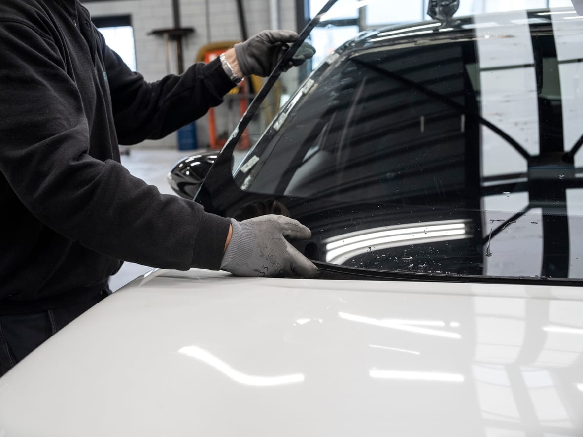 Technician in work gloves seating a new windshield into a white vehicle