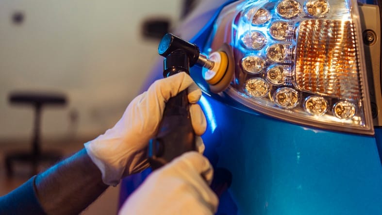 Polisher bringing up the gloss on the blue paint beside a car's tail light