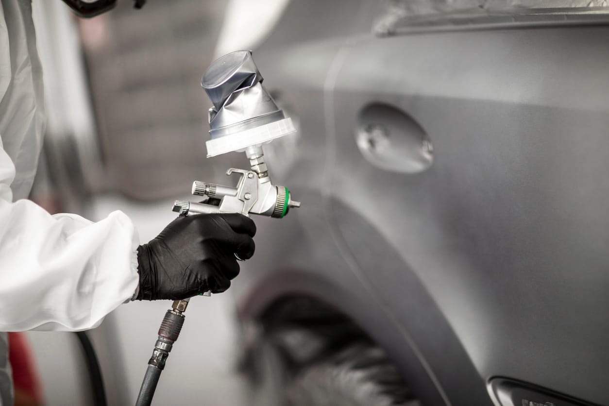 Gloved hand spraying an even coat of paint along a car body panel
